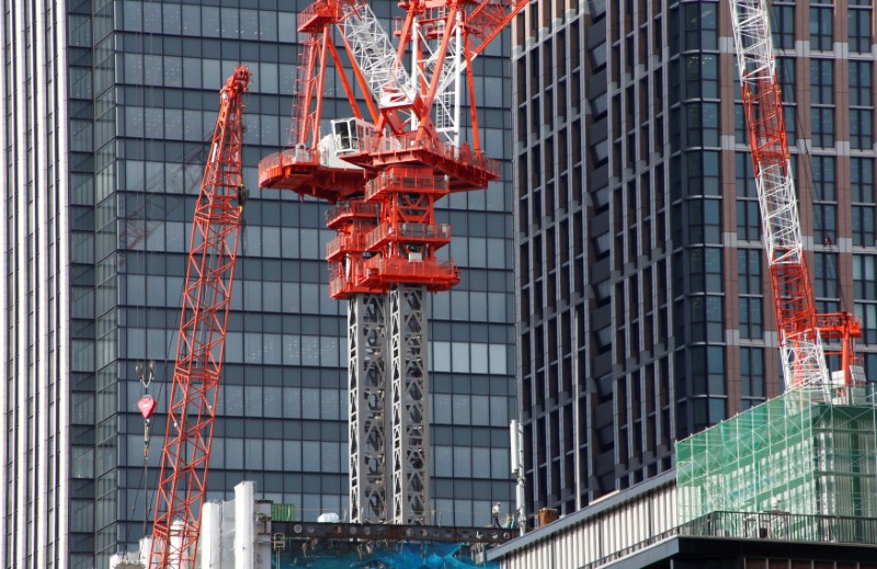 © Reuters. A worker walks underneath cranes at a construction site for a commercial building in Tokyo