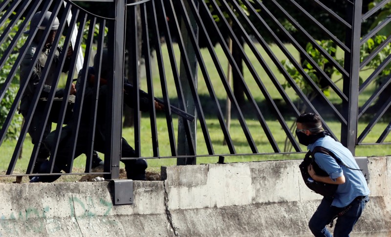 © Reuters. A member of the riot security forces points a gun through the fence at an opposition supporter during clashes at a rally against Venezuelan President Nicolas Maduro's government in Caracas