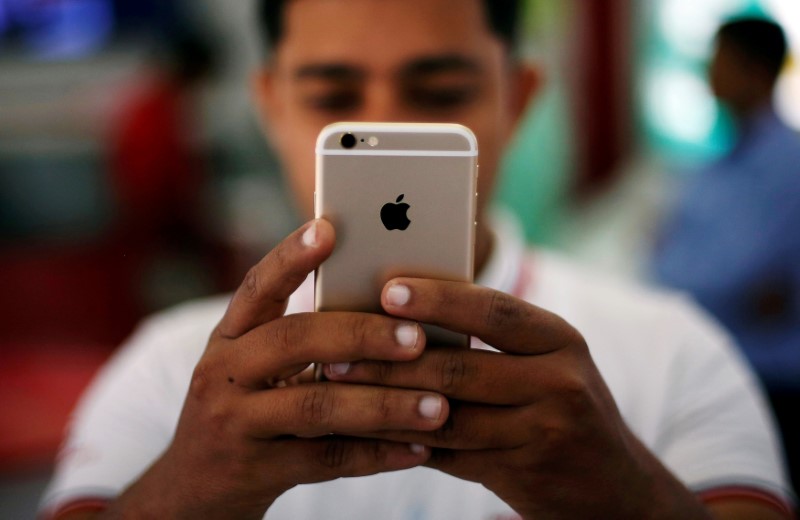 © Reuters. FILE PHOTO - A salesman checks a customer's iPhone at a mobile phone store in New Delhi