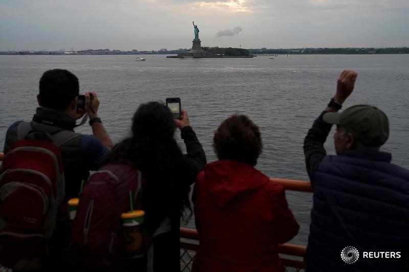 © Reuters. People take pictures of the Statue of Liberty as a man waves from the Staten Island Ferry as it rides between Staten Island and Manhattan in New York City