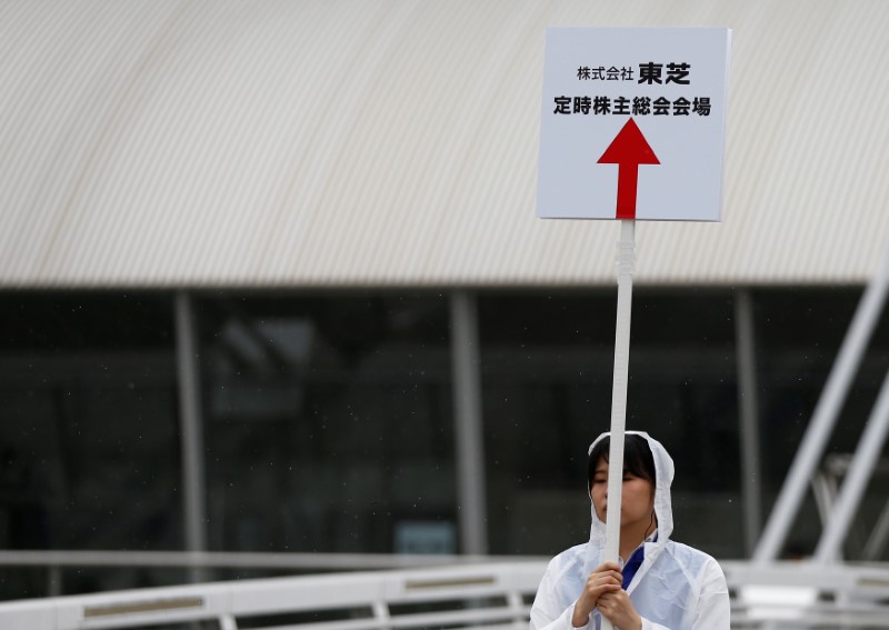 © Reuters. A staff member of Toshiba Corp. holds a sign board of the company's annual shareholders meeting at an entrance of the venue in Chiba, Japan