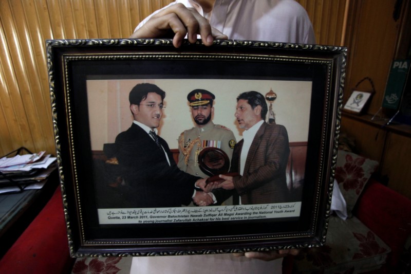 © Reuters. An image held by a colleague shows Pakistani journalist Zafarullah Achakzai (L), receiving a young journalist award from former Baluchistan Governor Nawab Zulfiqar Ali Magsi during a ceremony dated March 23, 2011, after his arrest in Quetta