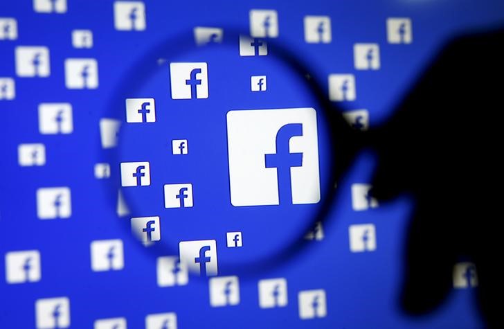 © Reuters. Pessoa posa com lupa diante de projeção de logos do Facebook