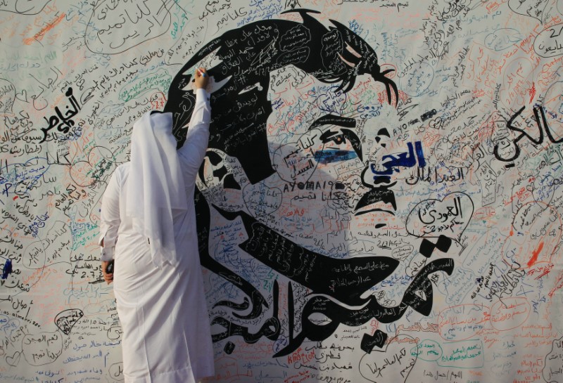 © Reuters. Man writes on a painting depicting Qatar’s Emir Sheikh Tamim Bin Hamad Al-Thani in Doha