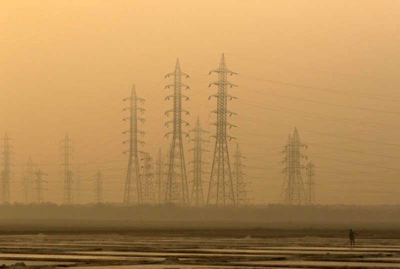© Reuters. FILE PHOTO - A worker levels a salt pan near electricity pylons in Mumbai