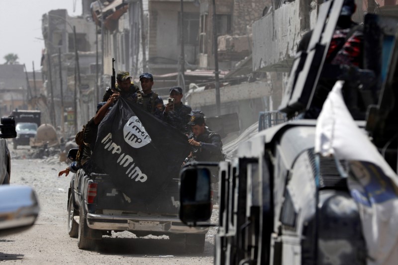 © Reuters. Iraqi Federal Police members hold an Islamic State flag which they pulled down during fighting between Iraqi forces and Islamic State militants in the Old City of Mosul