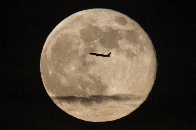 © Reuters. A silhouetted airplane flies past a 'super moon' over New York