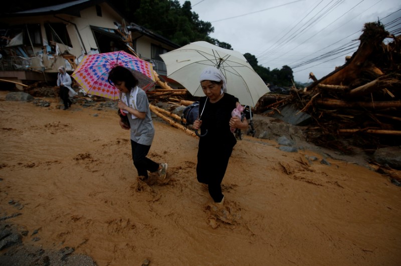 © Reuters. Local residents cross a destroyed road that is partially covered in floodwater as they evacuate from an isolated area at Haki district in Asakura