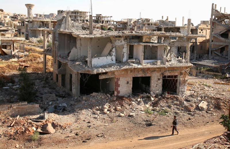 © Reuters. FILE PHOTO: A rebel fighter walks past damaged buildings in a rebel-held part of the southern city of Deraa