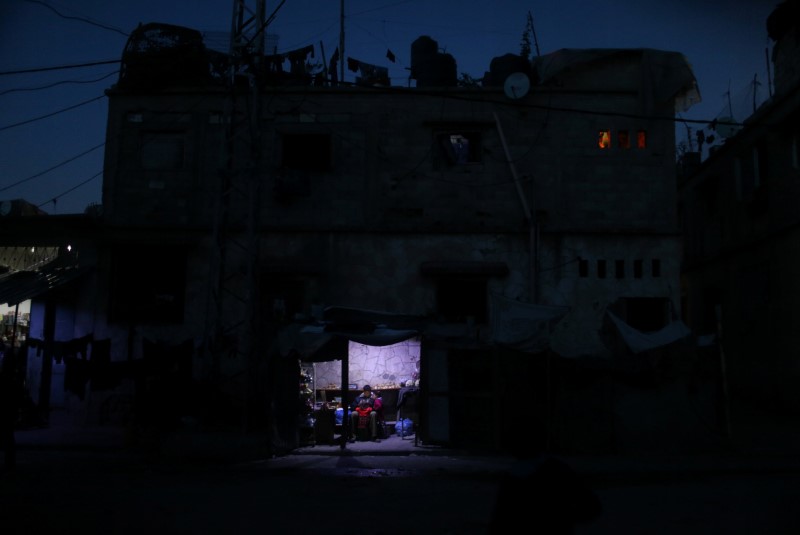 © Reuters. A Palestinian man sits as he sells vegetables in a makeshift shop lit with a lamp powered by a battery during a power cut in Beit Lahiya in the northern Gaza Strip