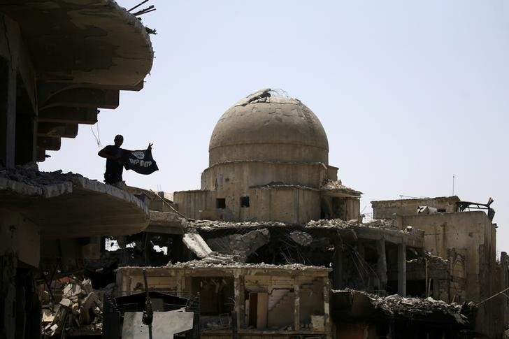 © Reuters. Membro das forças de segurança iraquianas segura a bandeira de militantes do Estado islâmico no topo de um edifício destruído em confrontos na Cidade Velha de Mosul, no Iraque