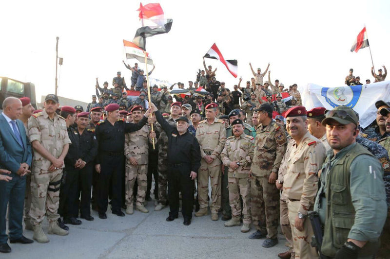 © Reuters. Iraqi Prime Minister Haider al-Abadi (C) holds an Iraqi flag as he announces victory over Islamic State in Mosul