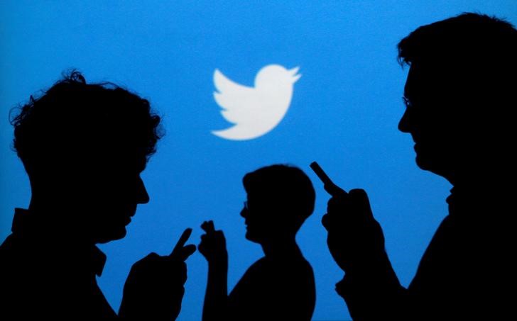 © Reuters. Pessoas usam celulares diante de logo do Twitter, uma das empresas que se manifestaram contra as mudanças nas regras de neutralidade da rede