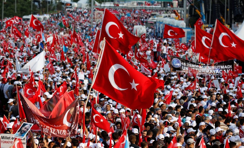 © Reuters. La gente agita banderas nacionales de Turquía mientras asisten a una ceremonia que marca el primer aniversario del intento de golpe en el Puente del Bósforo en Estambul