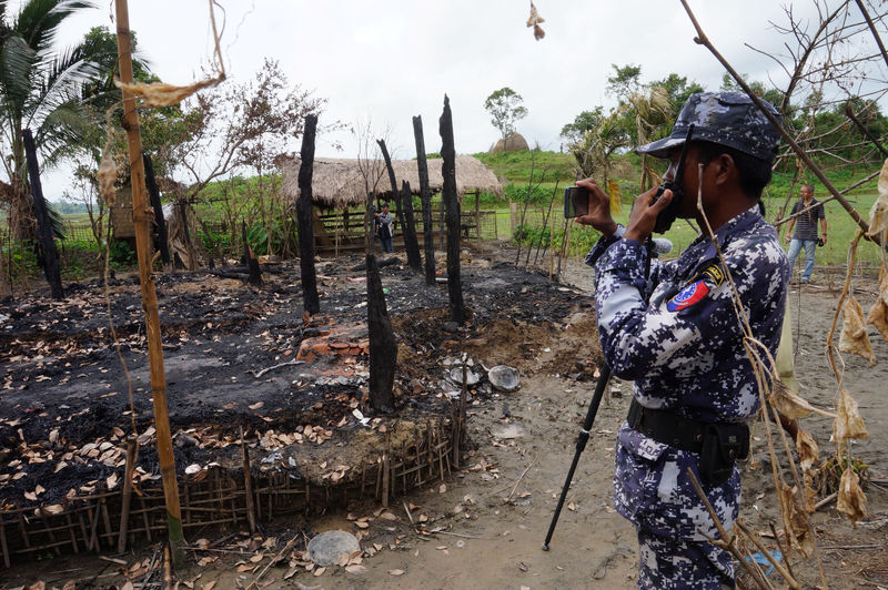 © Reuters. A Myanmar border guard police officer takes pictures at the remains of a burned house in Tin May village, northern Rakhine state, Myanmar