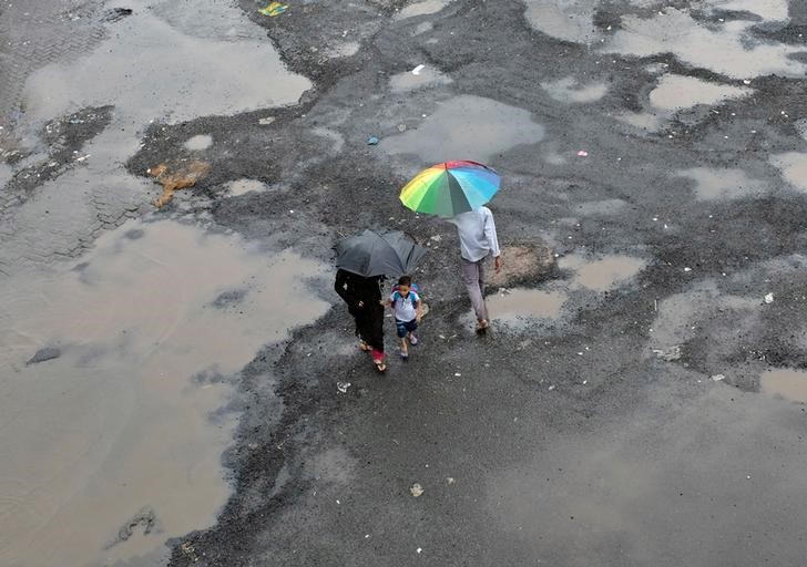 © Reuters. People carrying umbrellas cross a flooded street as it rains in Mumbai