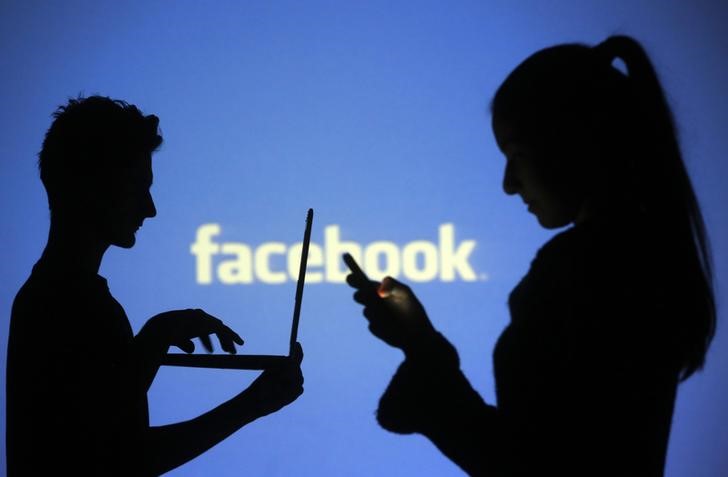 © Reuters. Pessoas usam eletrônicos diante de projeção do logo do Facebook