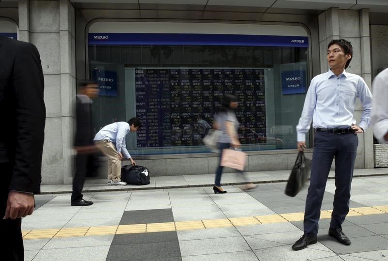 © Reuters. Passersby walk past in front of stock quotation board outside a brokerage in Tokyo