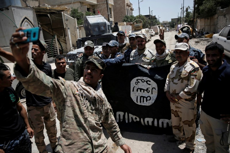 © Reuters. FILE PHOTO:Members of the Iraqi Army's 9th Armoured Division are photographed with an Islamic State flag, claimed after fighting with Islamic State militants in western Mosul