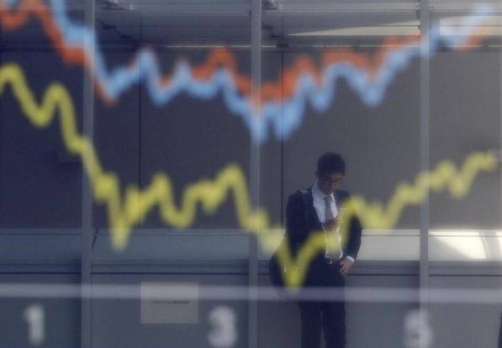 © Reuters. Отражение мужчины в экране с графиками динамики японского индекса Nikkei, Nasdaq Composite Index и Dow Jones Industrial Average