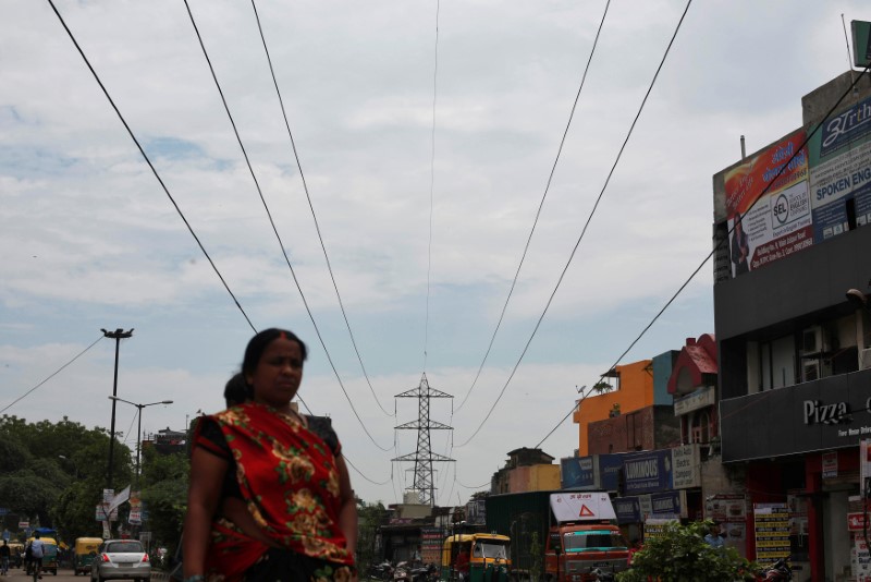 © Reuters. A woman walks under high-tension power lines near a coal-fired power plant in New Delhi