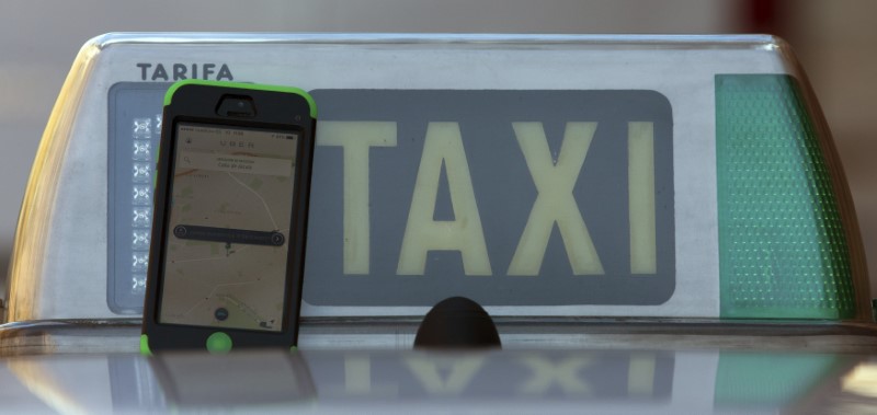 © Reuters. Photo illustration of car-sharing service app Uber on a smartphone next to a taxi sign in Madrid