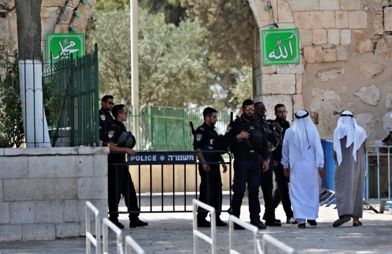 © Reuters. Palestinians walk next to Israeli security forces at the entrance of the compound known to Muslims as Noble Sanctuary and to Jews as Temple Mount in Jerusalem's Old City