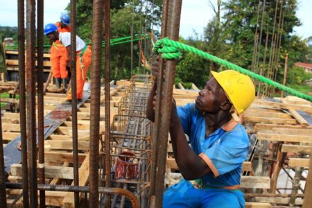 © Reuters. FILE PHOTO: A construction worker fastens metal bars on the rooftop of a new hospital under construction in Hoima