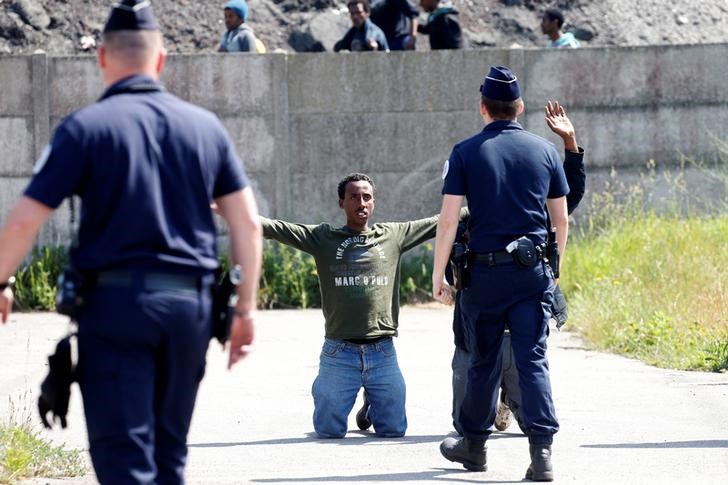 © Reuters. FILE PHOTO: French riot police walk towards a migrant who is on his knees as French authorities block their access to a food distribution point in Calais