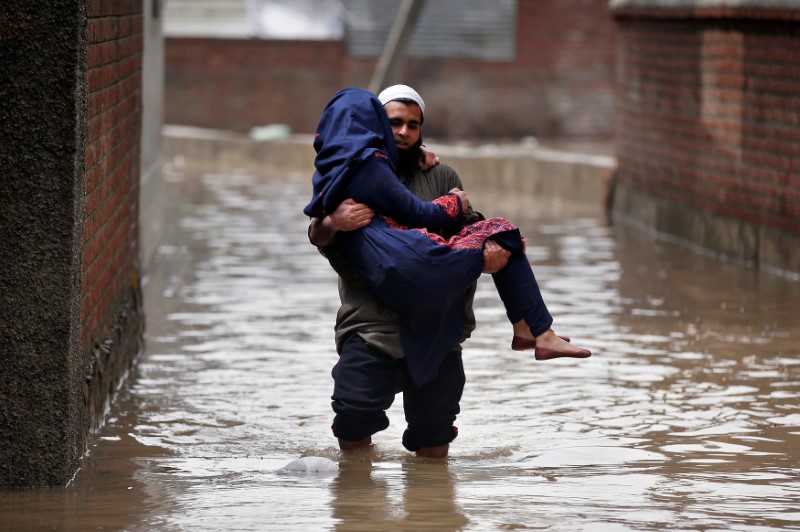 © Reuters. A man carries a woman as he wades through a flooded street after incessant rains in Srinagar