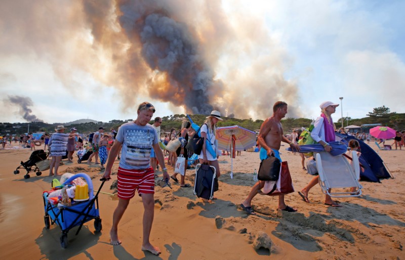 © Reuters. Turistas são removidos de praia devido a incêndio florestal em uma colina de Bormes-les-Mimosas, na França