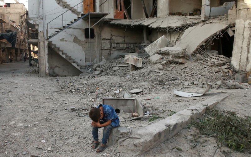 © Reuters. A boy sits near rubble of damaged buildings in Arbin, a town in the Damascus countryside