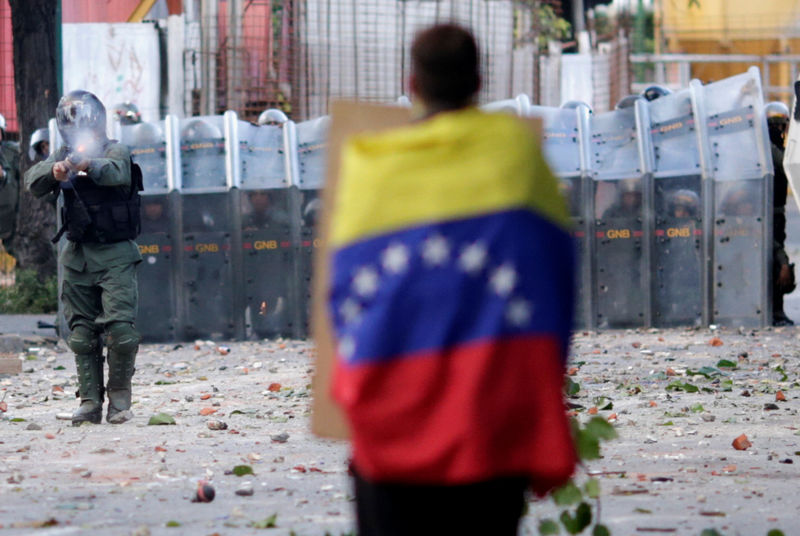 © Reuters. A man with a Venezuelan flag stands in front of riot security forces while rallying against Venezuela's President Nicolas Maduro's government in Caracas