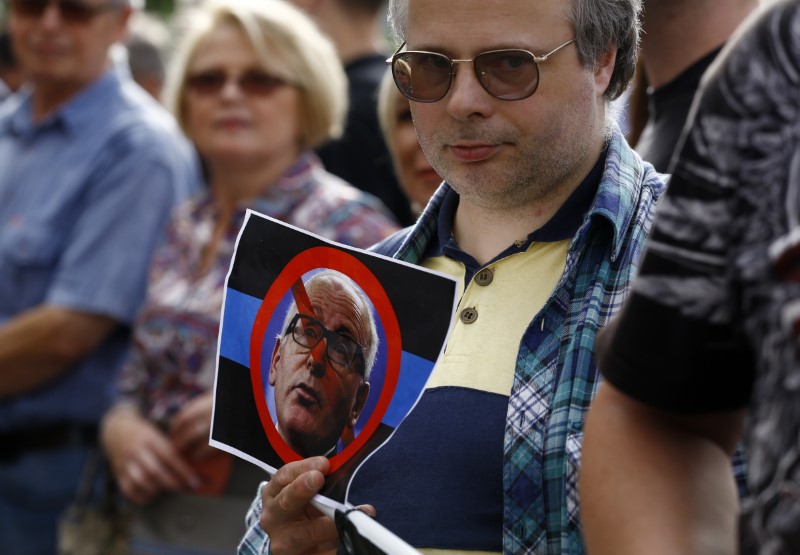 © Reuters. A man holds a picture of European Commission First Vice-President Frans Timmermans as he protests against EU plans to start legal action against Poland over judiciary reform, in front of European Commission Representation office, in Warsaw