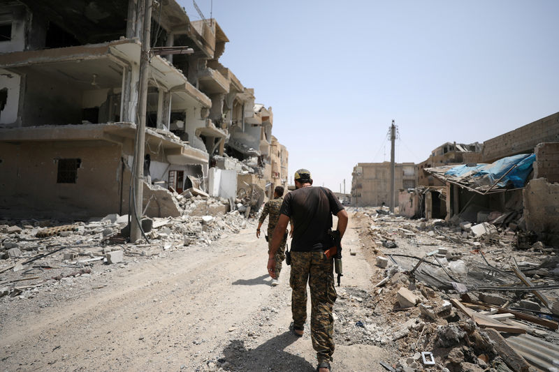 © Reuters. Fighters from Syrian Democratic Force (SDF) walk past damaged buildings in Raqqa city