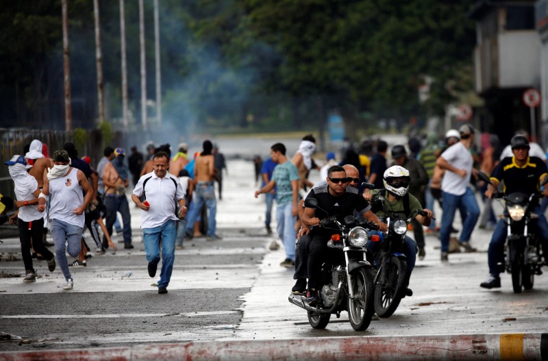 © Reuters. Demonstrators run and ride their motorcycles near Fuerte Paramacay military base during clashes with security forces in Valencia