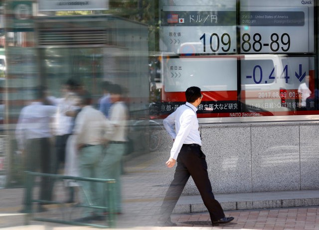 © Reuters. People walk past an electronic board showing exchange rate between Japanese Yen and U.S. Dollar outside a brokerage at a business district in Tokyo