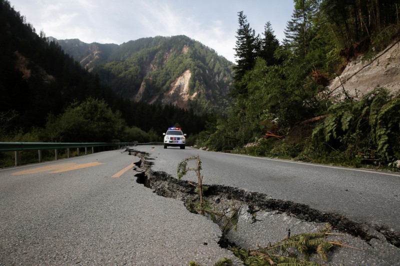 © Reuters. A crack runs through a mountain road as a police car approches after an earthquake outside Jiuzhaigou