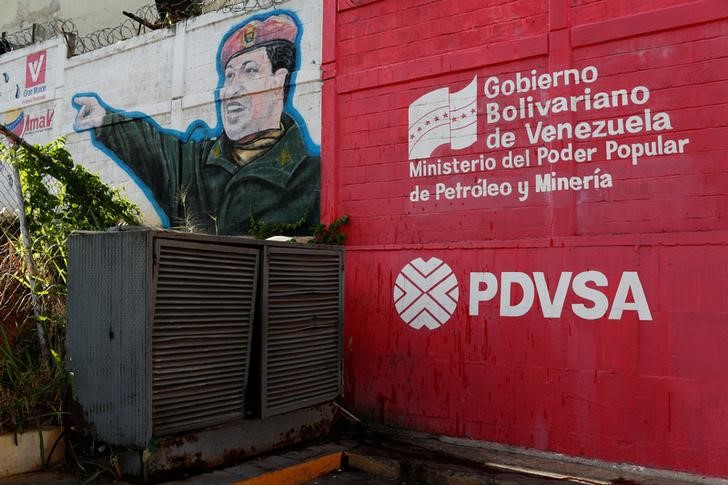 © Reuters. The logo of the Venezuelan state oil company PDVSA is seen next to a mural depicting Venezuela's late President Hugo Chavez at a gas station in Caracas