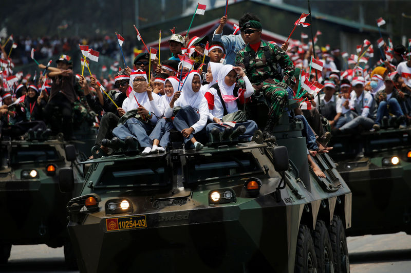 © Reuters. Students wave national flag as they sit on top of an armoured vehicle during celebrations for the 72nd anniversary of the Indonesia military, in Cilegon