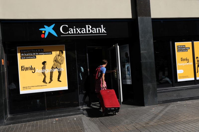 © Reuters. A man carrying a suitcase goes into a CaixaBank branch in Barcelona
