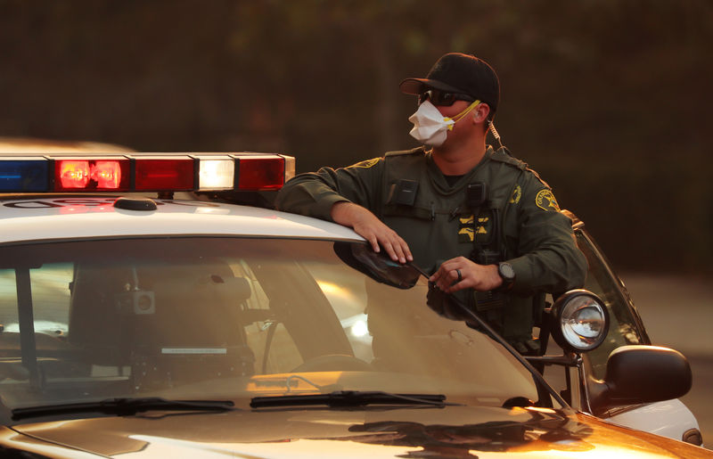 © Reuters. A police officer wears a mask for protection as he watches a wind driven wildfire in Orange, California