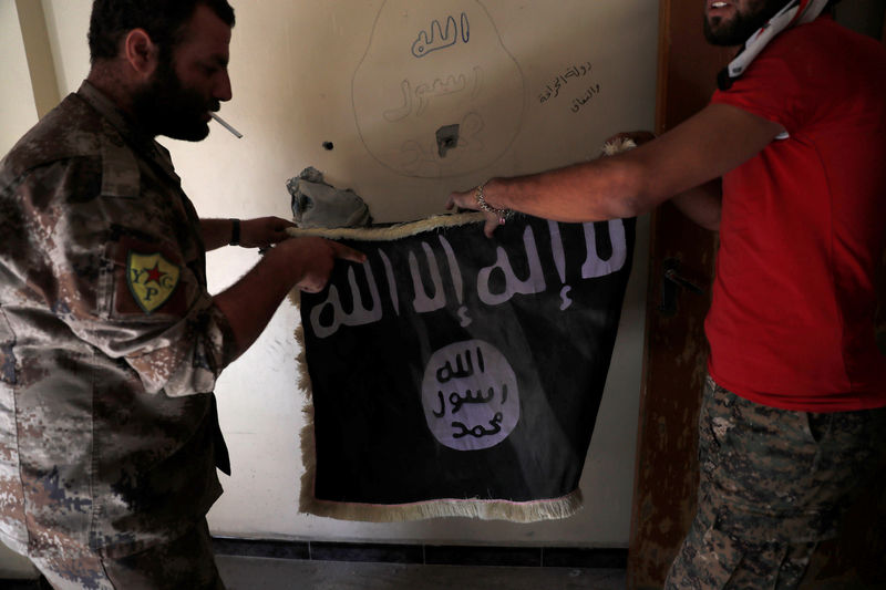 © Reuters. Members of Syrian Democratic Forces hold a flag of the Islamic State militants recovered at a building next to the stadium in Raqqa