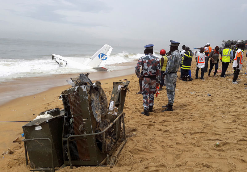 © Reuters. Policemen and rescuers stand near the wreckage of a propeller-engine cargo plane after it crashed in the sea near the international airport in Ivory Coast's main city, Abidjan