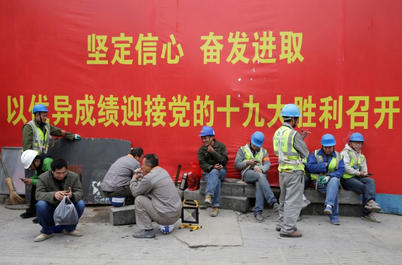 © Reuters. Workers rest in front of a banner promoting the 19th National Congress of the Communist Party of China in Beijing's business area