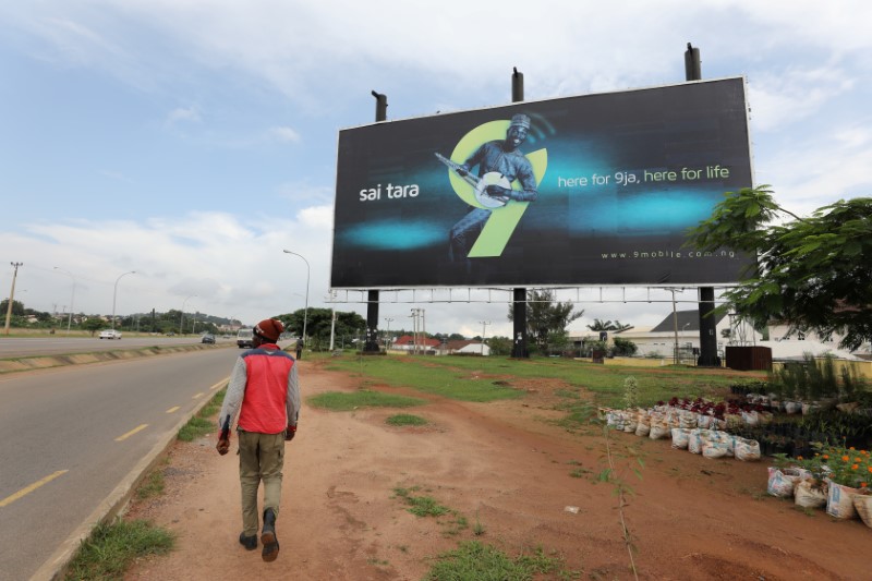 © Reuters. FILE PHOTO: A man walks towards a 9 Mobile telecom company outdoor billboard in Abuja