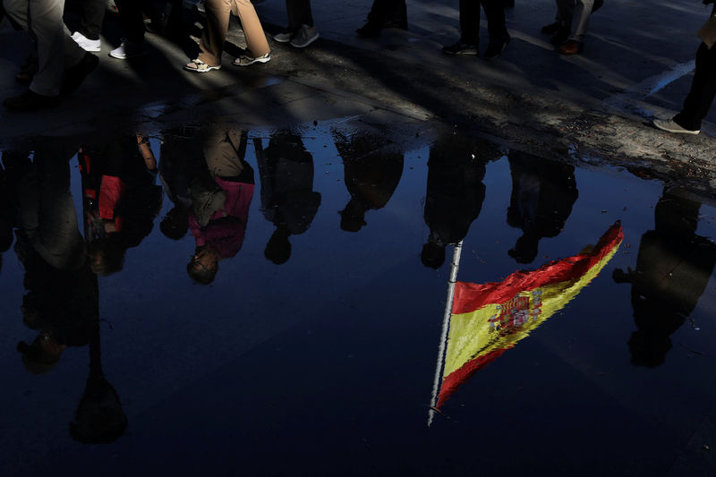 © Reuters. A Spanish flag and a group of tourists are reflected on a puddle of water in Plaza de Colon (Columbus Square) in Madrid