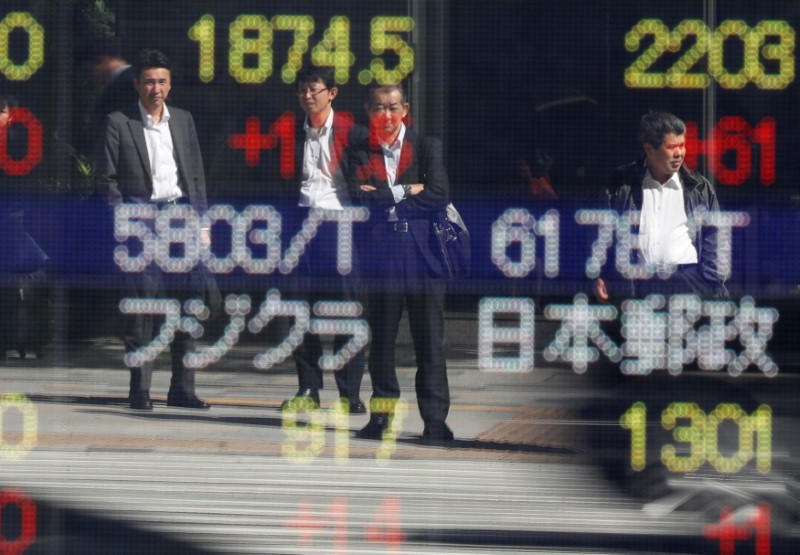 © Reuters. Passersby are reflected in an electronic stock quotation board outside a brokerage in Tokyo