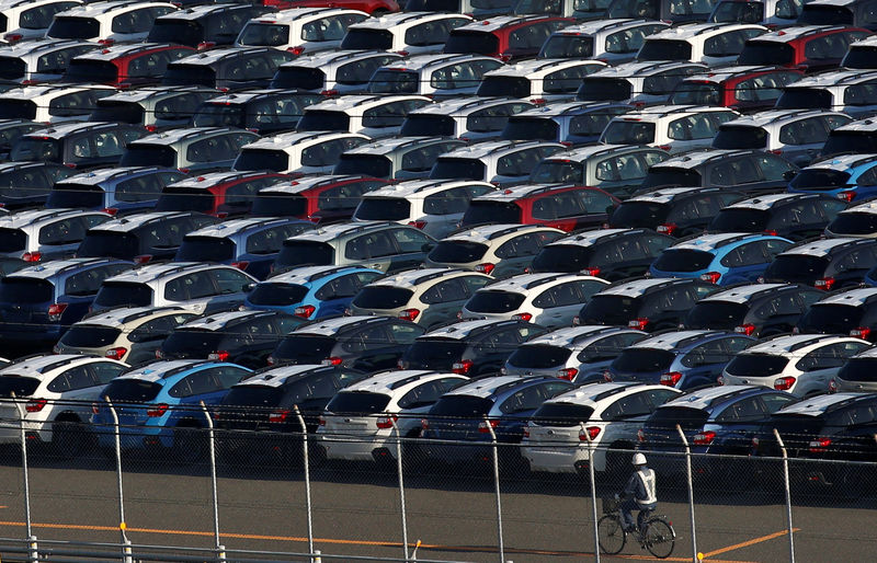 © Reuters. FILE PHOTO -  A worker in a bicycle drives past newly produced cars at an industrial port in Kawasaki