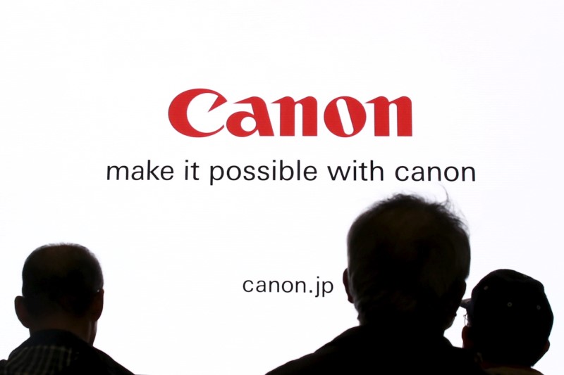 © Reuters. FILE PHOTO - People are silhouetted against a display of the Canon brand logo at CP+ camera and photo trade fair in Yokohama